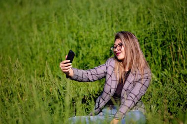Genç ve güzel Asyalı kız yazın çimenlerde selfie yapıyor.