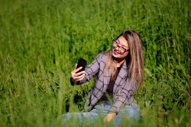 Genç ve güzel Asyalı kız yazın çimenlerde selfie yapıyor.