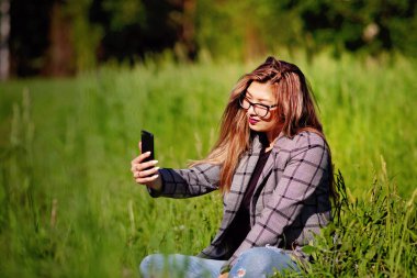 Genç ve güzel Asyalı kız yazın çimenlerde selfie yapıyor.