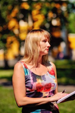 güzel sarışın kız bir yaz parkı ile yürür, bir defter ve kalem ile
