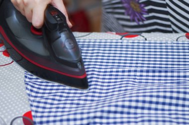 Ev hanımı ütü masasının üstündeki günlük kıyafetleri ütülüyor.