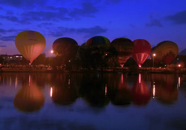 Hot air baloons flying in the evening sky near the lake — Stock Photo, Image