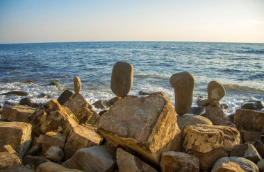 Yaz ve deniz dalgaları arka planında dengeli taşlar.