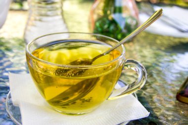 Açık havada kaşıkla şeffaf bardakta bir fincan bitki çayı. Dağlık bölgelerdeki otlardan çay