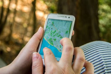 Kadın cep telefonundan haritalar çıkarıyor. Kadınların parmakları akıllı telefonu tutar ve dışarıdaki ekrana dokunur.