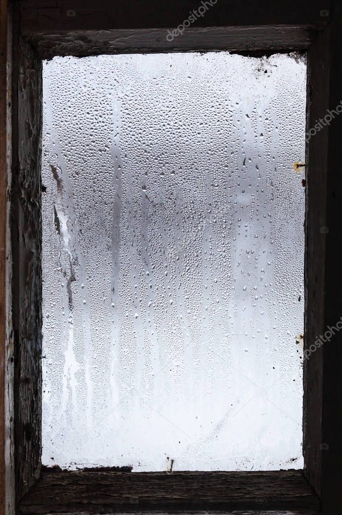 water from melting ice on surface of misted window in old rural house in winter