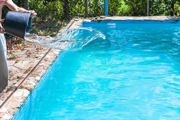 男子在乡下屋后院的室外游泳池里从水桶里倒出消毒剂 — 图库照片