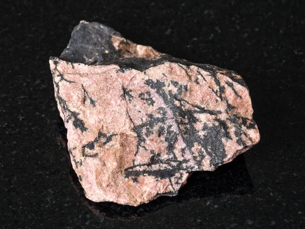 stock image macro shooting of natural mineral - rough Rhodonite stone on black granite from Ural Mountains