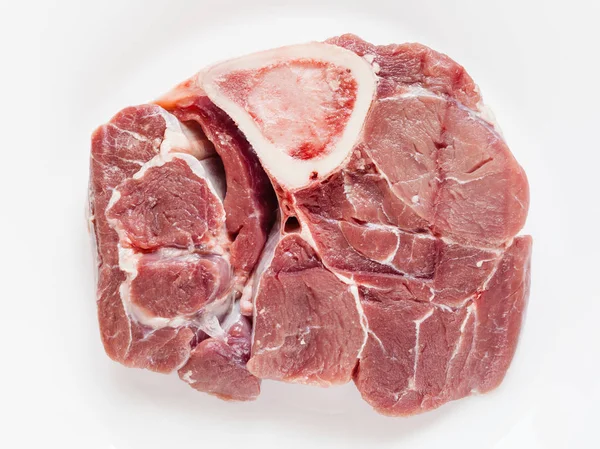 イタリア料理オッソブーコ白い皿の上に Marrowbone と生の子牛の肉のスライスの平面図 — ストック写真