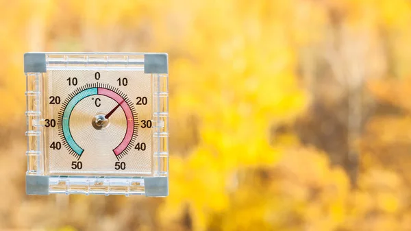 outdoor thermometer on home window and blurred yellow forest on background in sunny warm autumn day