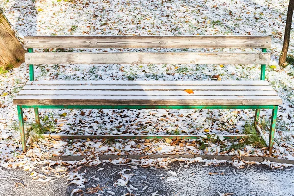 在寒冷的秋日 城市花园的第一层雪覆盖着木制的长凳 — 图库照片