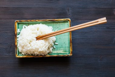 koyu ahşap tahta üzerinde yeşil tabakta yemek çubukları ile haşlanmış pirinç üstten görünüm