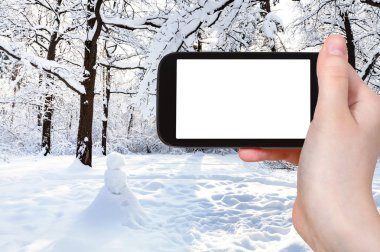 seyahat konsepti - kardan adamın karla kaplı çayırdaki turistik fotoğrafları Moskova 'da kış aylarında şehir parkının meşe koruluğunda akıllı telefonuyla boş ekran ve reklam için boş yer.
