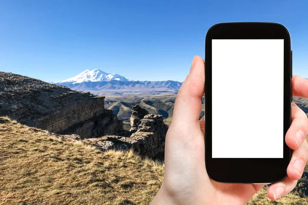 旅行概念 伯玛米特高原悬崖的旅游照片和俄罗斯北高加索山脉的埃尔布鲁斯山的看法在智能手机与削减屏幕与空白的地方广告 — 图库照片