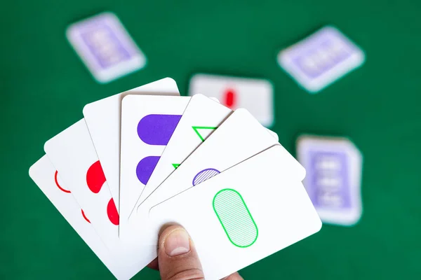 Player holds Set game cards over green table — Stock Photo, Image