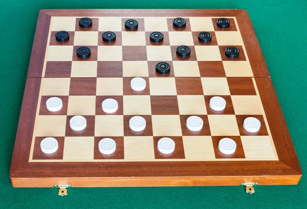 Checkers on wooden board on green table — Stock Photo, Image