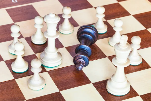 Чёрный король шахмат в окружении белых фигур — стоковое фото