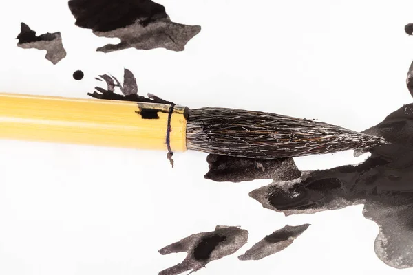 Black painted tip of paintbrush over ink blots — Stock Photo, Image