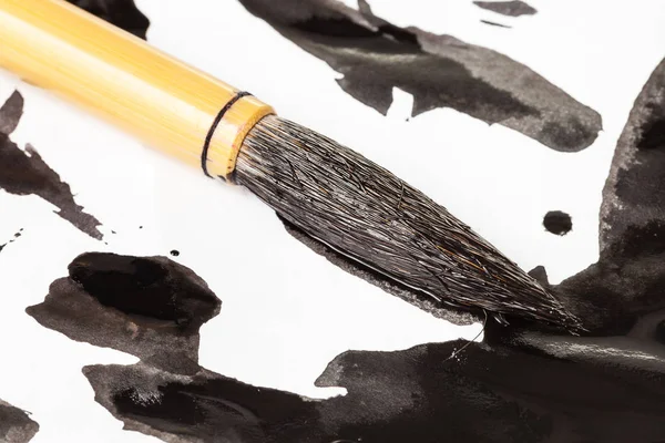 Black tip of paintbrush over ink spots close up — Stock Photo, Image