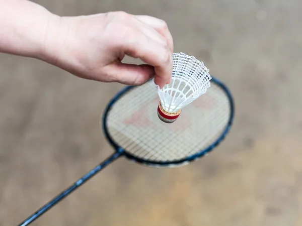 Hand with white shuttlecock over badminton racquet — Stock Photo, Image