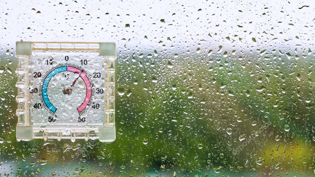raindrops and outdoor wet thermometer on glass