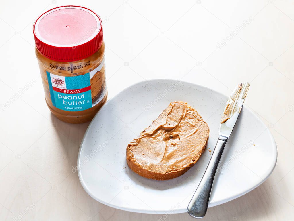 MOSCOW, RUSSIA - JUNE 16, 2020: closed jar of Hy-Top creamy Peanut butter and toast with spread on plate on table. HyTop is brand of private label groceries created in the 1950 in Illinois, USA