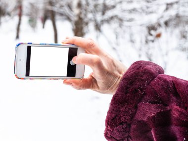 Kadın eli, kış ormanlarında kesme ekranlı akıllı telefonla fotoğraf çeker.