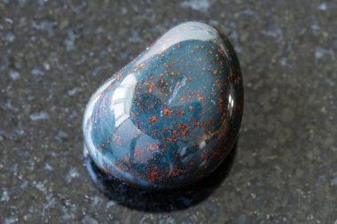 Jeolojik koleksiyondaki doğal mineral örneklerinin makro fotoğrafçılığı - siyah granit arka planda yuvarlanan Heliotrope (Kan Taşı) taşı