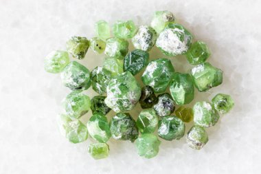 sample of many raw demantoid crystals on white marble background close up from Ural Mountains, Russia