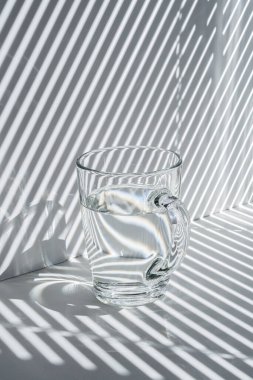 Beyaz arka planda bir bardak su ve çizgili gölge.