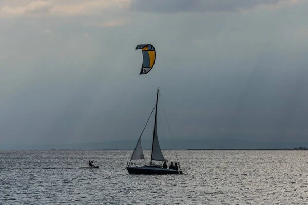 帆船与风筝冲浪者在湖面相遇 — 图库照片