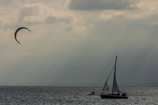 Segelbåt Och Kitesurfare Vid Sjö Med Moln Och Solstrålar — Stockfoto