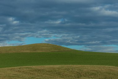 Tepeli yeşil manzara ve bulutlu gökyüzü
