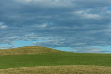 İlkbaharda tepeleri ve bulutları olan yeşil bir manzara.