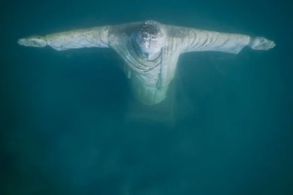 jesus statue from above while diving in a lake in the mountains