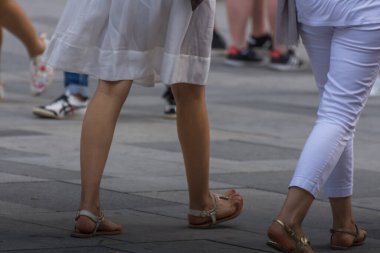 Şehirde beyaz elbiseli ve sandaletli genç bir kadın var.