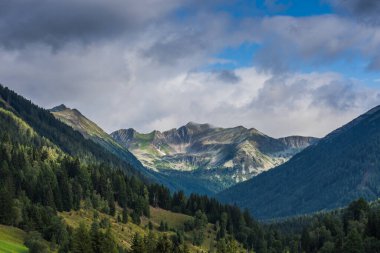 Gökyüzünde bulutlar ve ormanlarla dolu renkli dağlar