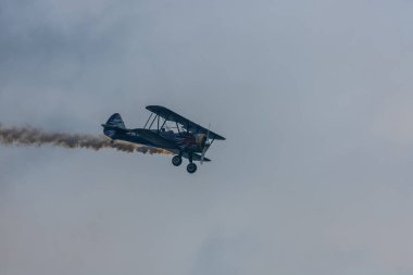 Çift kanatlı uçak yağmur bulutlu bir hava gösterisinde dumanla uçar.