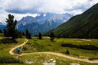 Tourist cycling in Cortina d'Ampezzo, stunning rocky mountains on the background. Man riding MTB enduro flow trail. South Tyrol province of Italy, Dolomites. clipart