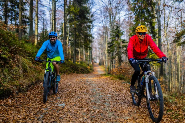 Cycling, mountain biker couple on cycle trail in autumn forest. Mountain biking in autumn landscape forest. Man and woman cycling MTB flow uphill trail.