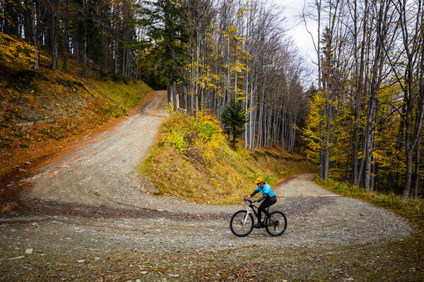 Mountain biking woman riding on bike in autumn mountains forest landscape. Woman cycling MTB flow trail track. Outdoor sport activity.