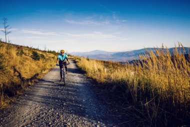 Bisikletli kadın, sonbahar ormanı manzarasında bisiklet sürüyor. MTB akış yolu üzerinde bisiklet süren bir kadın. Açık hava sporları aktivitesi.