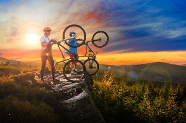 Bisikletli kadın ve erkekler günbatımı dağ manzarasında bisiklet sürüyorlar. Birkaç bisiklet MTB enduro akış yolu. Açık hava sporları aktivitesi.