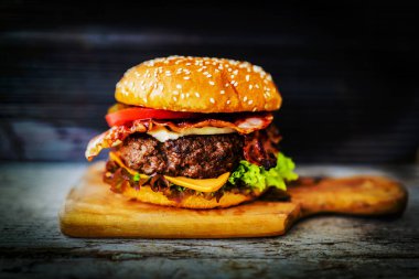 Lezzetli füme ızgara ve sırlı sığır eti burger marul, peynir ve domuz pastırması boşaltmak, duman mesquite ahşap ahşap arka plan ile ahşap masa üzerinde patates kızartması ile servis.