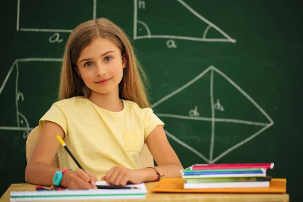 Back to school.. Funny beatifull girl sitting in the clasroom against blacboard. Child in school with book and accessories. Education concept