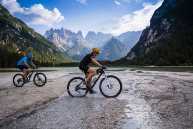 Tourist cycling in Cortina d'Ampezzo, stunning rocky mountains on the background. Family riding MTB enduro flow trail. South Tyrol province of Italy, Dolomites. clipart
