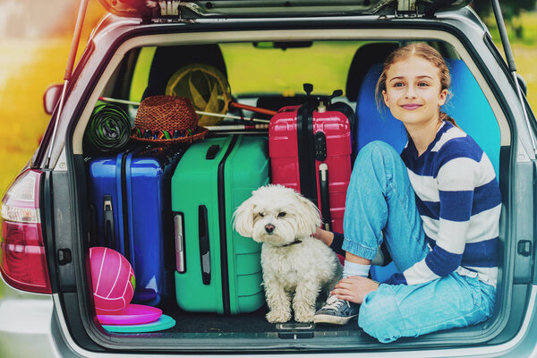 Summer vacation, young girl in car trunk with dog in the car is ready for travel for family vacation.
