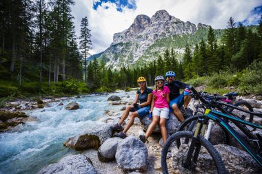Tourist cycling in Cortina d'Ampezzo, stunning rocky mountains on the background. Family riding MTB enduro flow trail. South Tyrol province of Italy, Dolomites. clipart