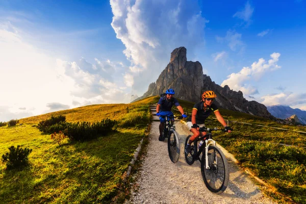 Cycling woman and man riding on bikes in Dolomites mountains landscape. Couple cycling MTB enduro trail track. Outdoor sport activity.