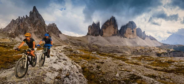 Cycling woman and man riding on bikes in Dolomites mountains andscape. Couple cycling MTB enduro trail track. Outdoor sport activity.